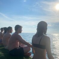 Fünf Personen sitzen in Badekleidung am Mittelmeer und genießen den strahlenden Sonnenschein.